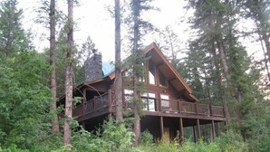 A cabin with a wooden deck and a stone chimney, surrounded by tall trees. - Great All Season Log House in Alpine,WY (Alpine)