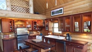 A rustic wooden cabin interior with a kitchen featuring wooden cabinets, a central island with stools, and a large window providing natural light. - Great All Season Log House in Alpine,WY (Alpine)