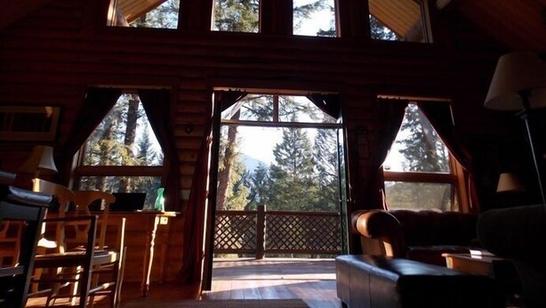 A log cabin interior with a high ceiling, multiple windows, and a view of a forest. - Great All Season Log House in Alpine,WY (Alpine)