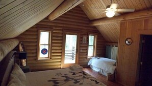 A cozy attic bedroom with a sloped ceiling, a bed with a floral bedspread, a small table with a lamp, and a ceiling fan. - Great All Season Log House in Alpine,WY (Alpine)