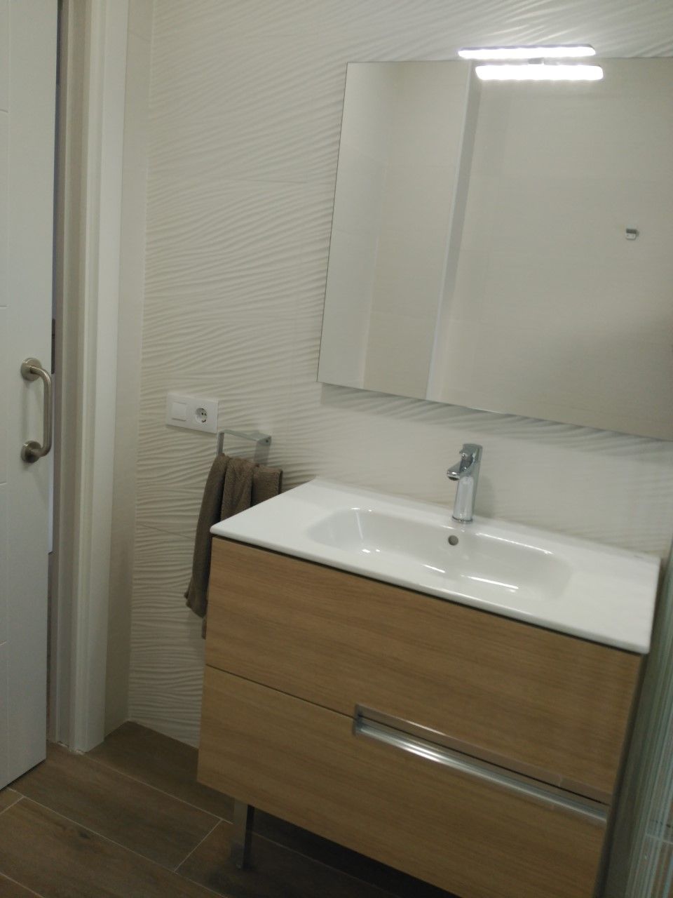 Un baño con un lavabo blanco, un espejo y una toalla colgada en la pared.