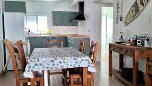 Una cocina moderna con armarios verde mar, una isla central y una mesa de comedor con mantel estampado.
