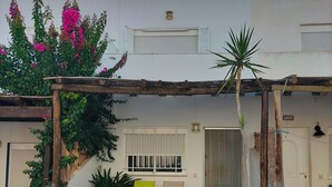 Un edificio residencial de fachada blanca, una cerca de madera en primer plano y un balcón con mesa y sillas.