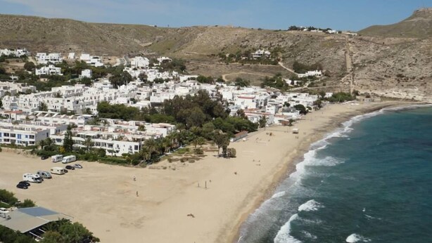 Un pueblo costero con edificios blancos, una playa de arena y una ladera rocosa.