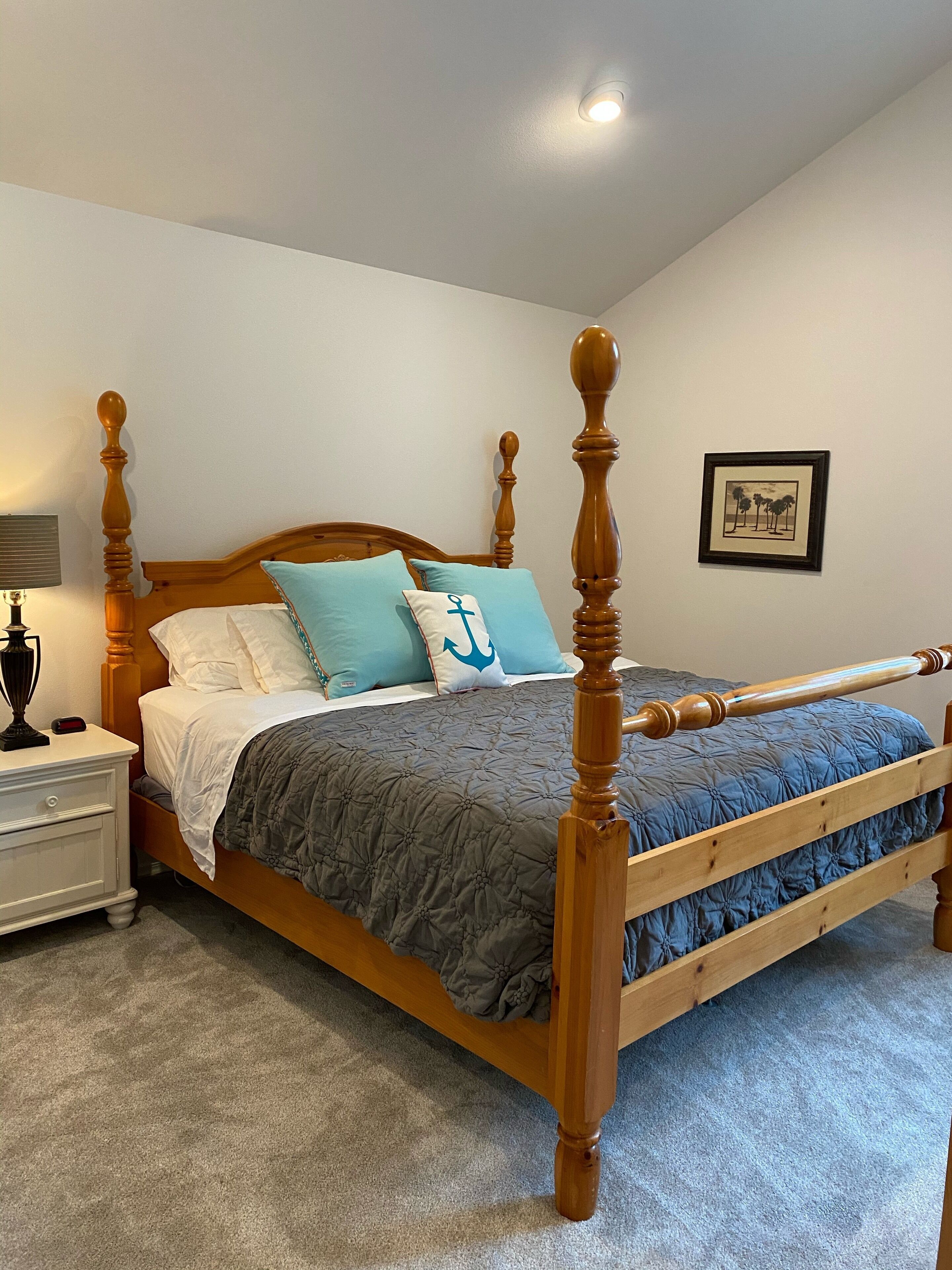 Una cama con dosel de madera, un edredón acolchado gris y dos almohadas con un diseño de ancla azul.