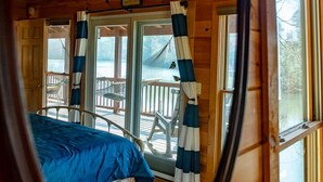Een houten kamer met een bed, een raam met gordijnen en uitzicht op het buitendek.
