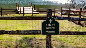 Een bord voor Selah's Retreat met uitzicht op een meer en een steiger op de achtergrond.