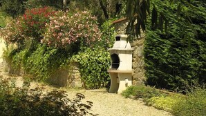 Um jardim com uma estrutura de pedra, possivelmente uma fonte ou elemento decorativo, rodeado por vegetação exuberante e plantas floridas.