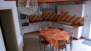 Ett kök med vita skåp, kakel på väggen ovanför arbetsbänken, ett matbord med stolar och en hängande lampa.