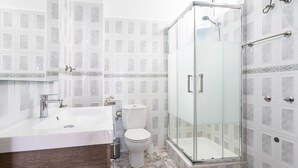 Un baño con ducha de vidrio, lavamanos blanco y retrete.