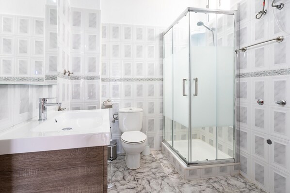 A bathroom with a glass-enclosed shower, a white sink, and a toilet.