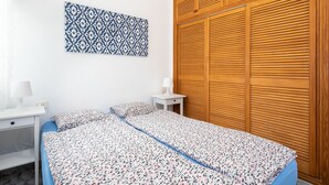 Un dormitorio con dos camas, un armario de madera, una mesita de noche con lámpara y un tapiz decorativo en la pared.