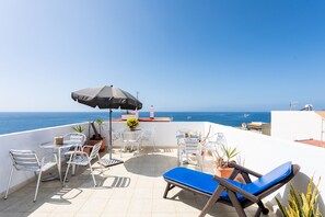 A terrace with a table, chairs, a blue lounge chair, and a potted plant.