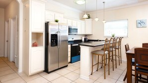 Una cocina con armarios blancos, electrodomésticos de acero inoxidable y una zona de comedor con sillas de madera.