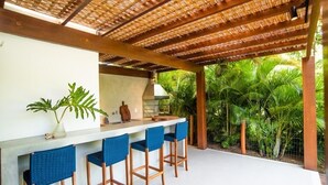 Un espace bar en plein air doté d’un toit de chaume, de chaises en bois et offrant une vue sur une végétation luxuriante.