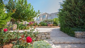 A courtyard with stone pathways, lush greenery, and a building with balconies. - Villas For Family Holidays (Rethymno)