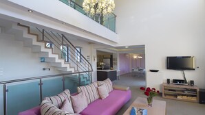 A modern living room with a pink sofa, a staircase, a kitchen, and a dining area. - Villas For Family Holidays (Rethymno)