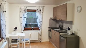 Et kompakt køkken med spiseplads, med et vindue med gardiner, en radiator, en vask, en komfur og et køleskab.