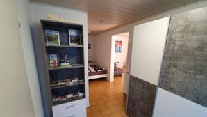 A hallway with a bookshelf labeled "Welcome" and a bed with a patterned bedspread.