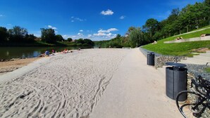 En sandstrand med en klar blå himmel, en flod og et græsareal med mennesker og en cykel.