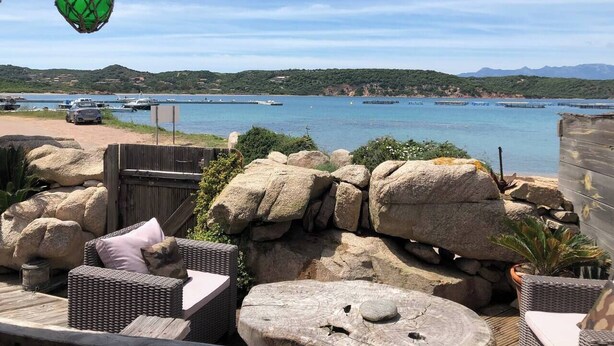 A patio area with wicker furniture, large rocks, and a view of a marina and hills. - L'Abri des flots Seaside Villa in Bonifacio, L'Abri des flots (Bonifacio)