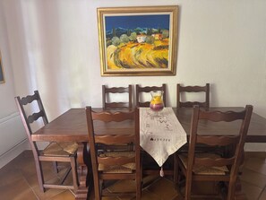 A dining table with a painting above it, surrounded by wooden chairs with woven seats. - St Raphael Garden Villa very nice and quiet close to the beaches and Centre (Saint-Raphaël)