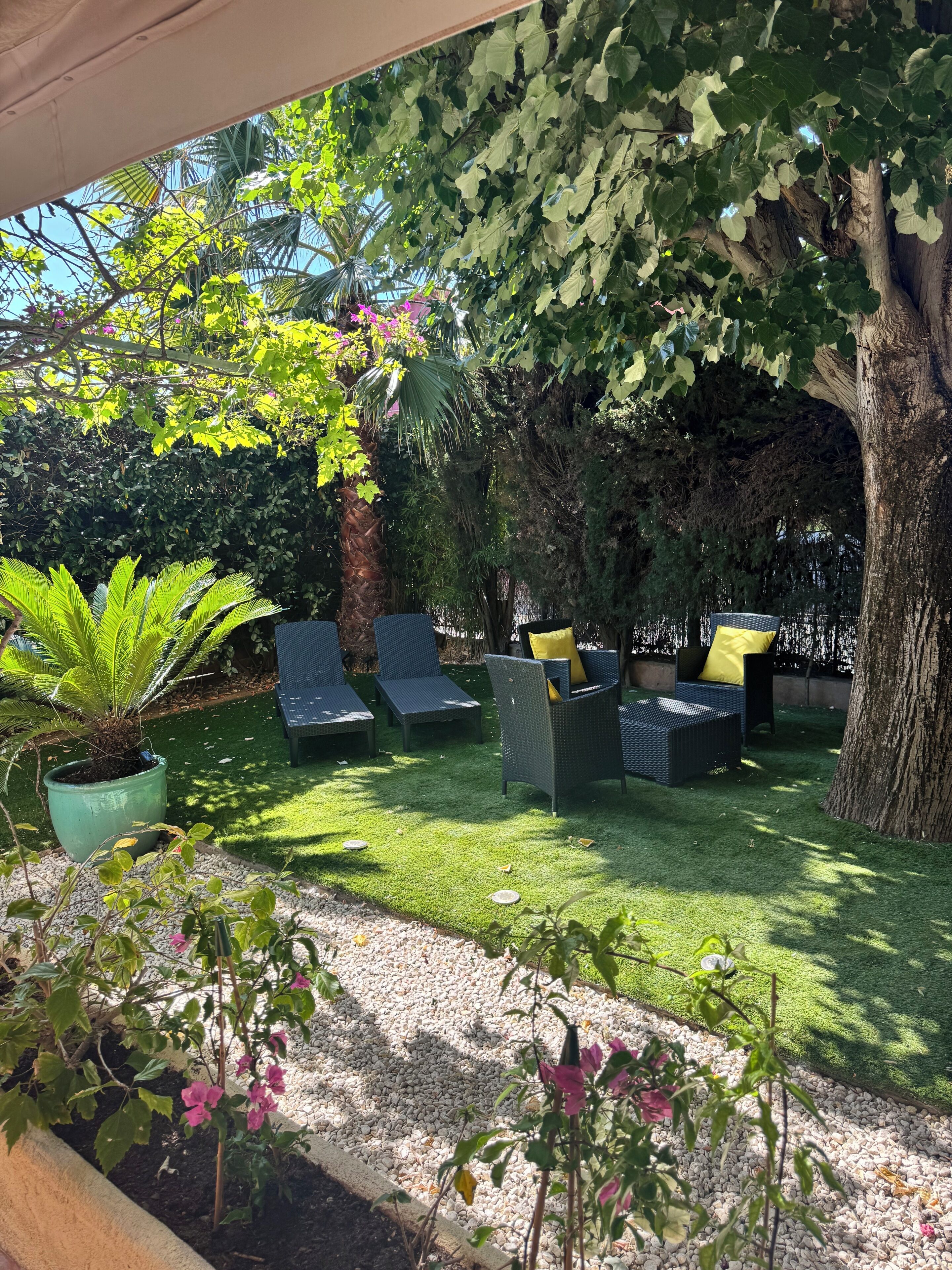 A garden area with artificial grass, a large tree, and outdoor seating with cushions.