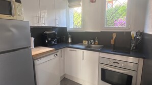 Une cuisine compacte avec des meubles blancs, un four à micro-ondes encastré, une machine à café et une fenêtre donnant sur un espace verdoyant.