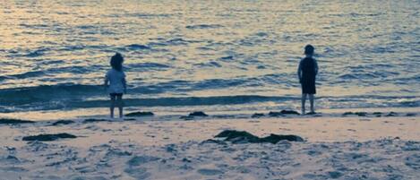A beach with two people standing at the water's edge.
