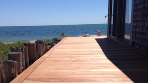 A wooden deck leading to a beach with a clear view of the ocean and a building with large windows. - Private Sandy Beach, Truly Oceanfront,Private Decks, Free Kayak, Sleeps  5 (South Yarmouth)
