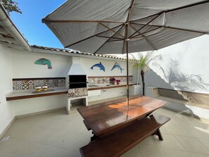 En udendørs terrasse med et træbord, en grill og en stor parasol.
