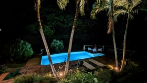 Ein Nachtblick auf einen Swimmingpool, umgeben von Palmen und einer Holzterrasse.