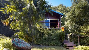 Ein Baumhaus mit Holzfassade, umgeben von dichtem Grün und einer kleinen Treppe, die hinauf führt.