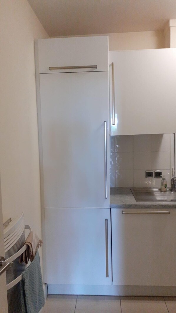 Une cuisine avec un réfrigérateur blanc, un évier et un mur recouvert de carreaux.