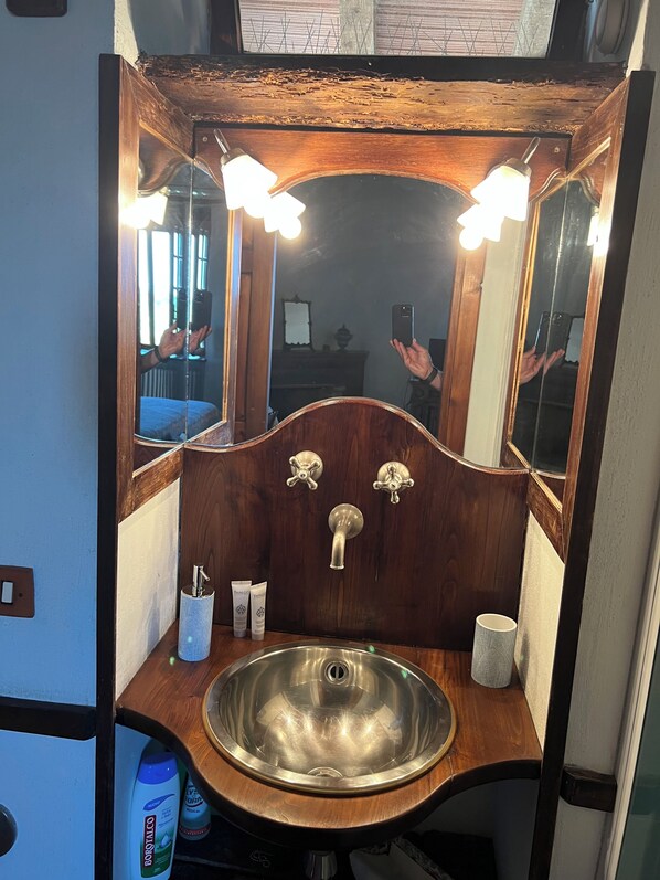 Un baño con tocador de madera, lavamanos de acero inoxidable y espejo con iluminación.