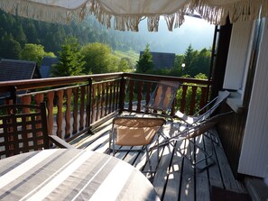 Een balkon met houten hekwerk, een tafel en twee stoelen.