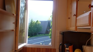 A kitchen with wooden cabinets, a window with a view of the street, a coffee maker, and a kettle. - SUPER LIORAN INDIVIDUAL CHALET COMFORTABLE 8 BEDS (Laveissière)