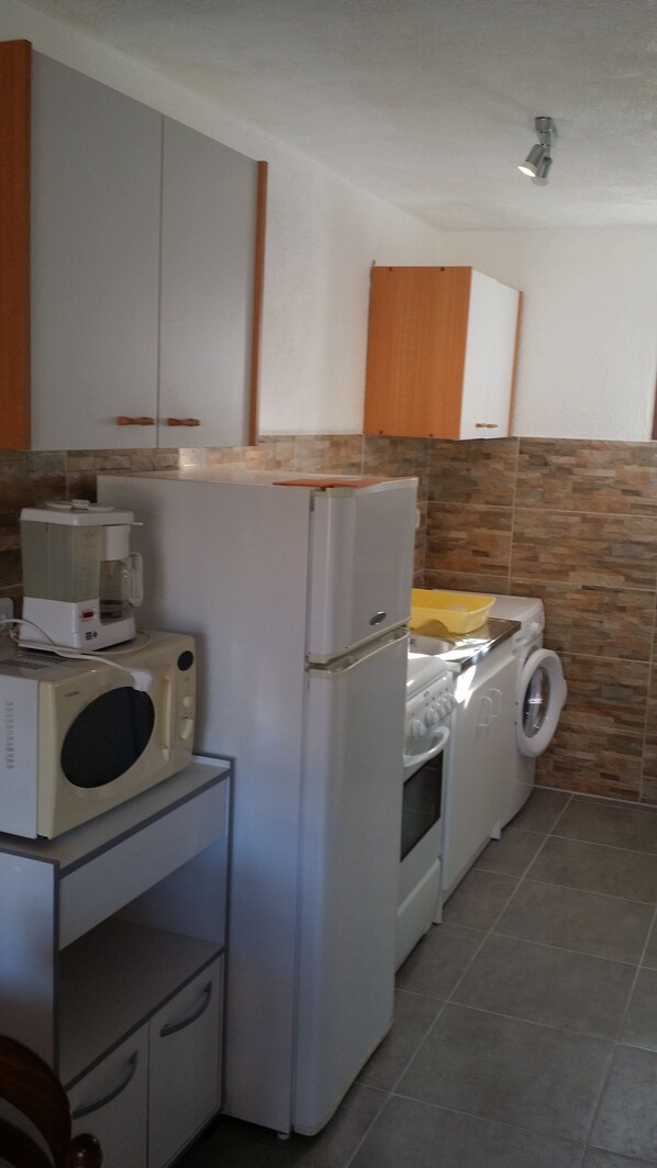 A compact kitchen with a refrigerator, microwave, and washing machine.