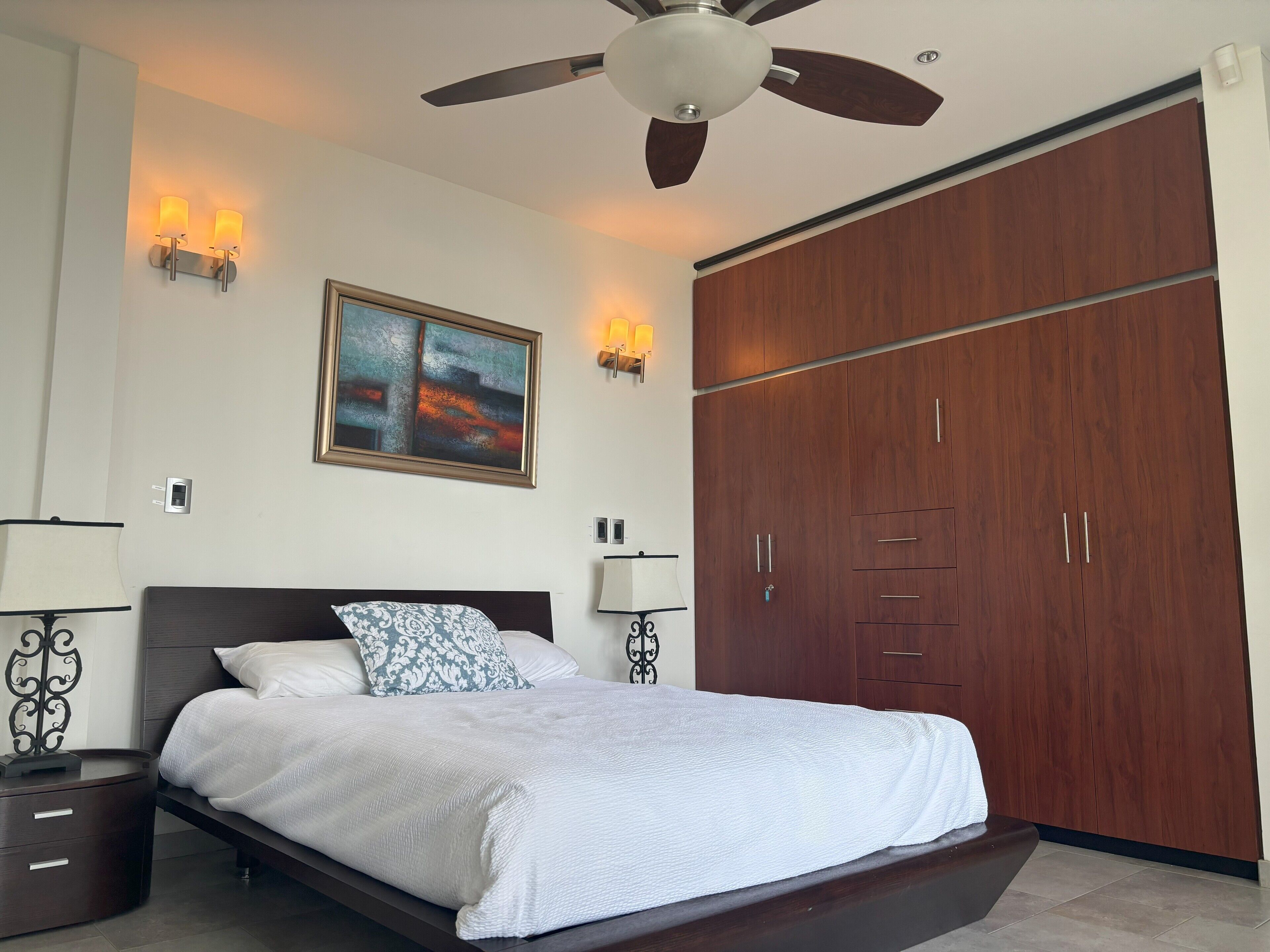 Een slaapkamer met een bed, een plafondventilator, een kledingkast en wandlampen.