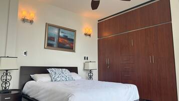 Een slaapkamer met een bed, een plafondventilator, een kledingkast en wandlampen.