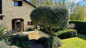 A stone house with a wooden door, a small patio with a table and chairs, and a well-maintained garden with a large bush and trimmed hedges. - ACABANES Luxury Dordogne villas, 20m Bergerac airport, 5m Chateau Vigiers golf (Thénac)