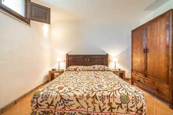 Un dormitorio con una cama de madera, dos lámparas de noche, un armario de madera y una ventana con vistas al cielo.