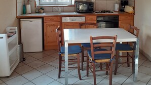 Une cuisine avec des meubles de rangement en bois, un réfrigérateur blanc, une cuisinière, un four à micro-ondes et une table à manger avec des chaises.