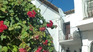 A person holding a green mug, standing in front of a white building with a balcony and red flowers. - Burriana Beach 4 Mins Walk, Spanish Town House, 2 Pools - Gardens, WIFI, Air-Con (Burriana, Malaga)