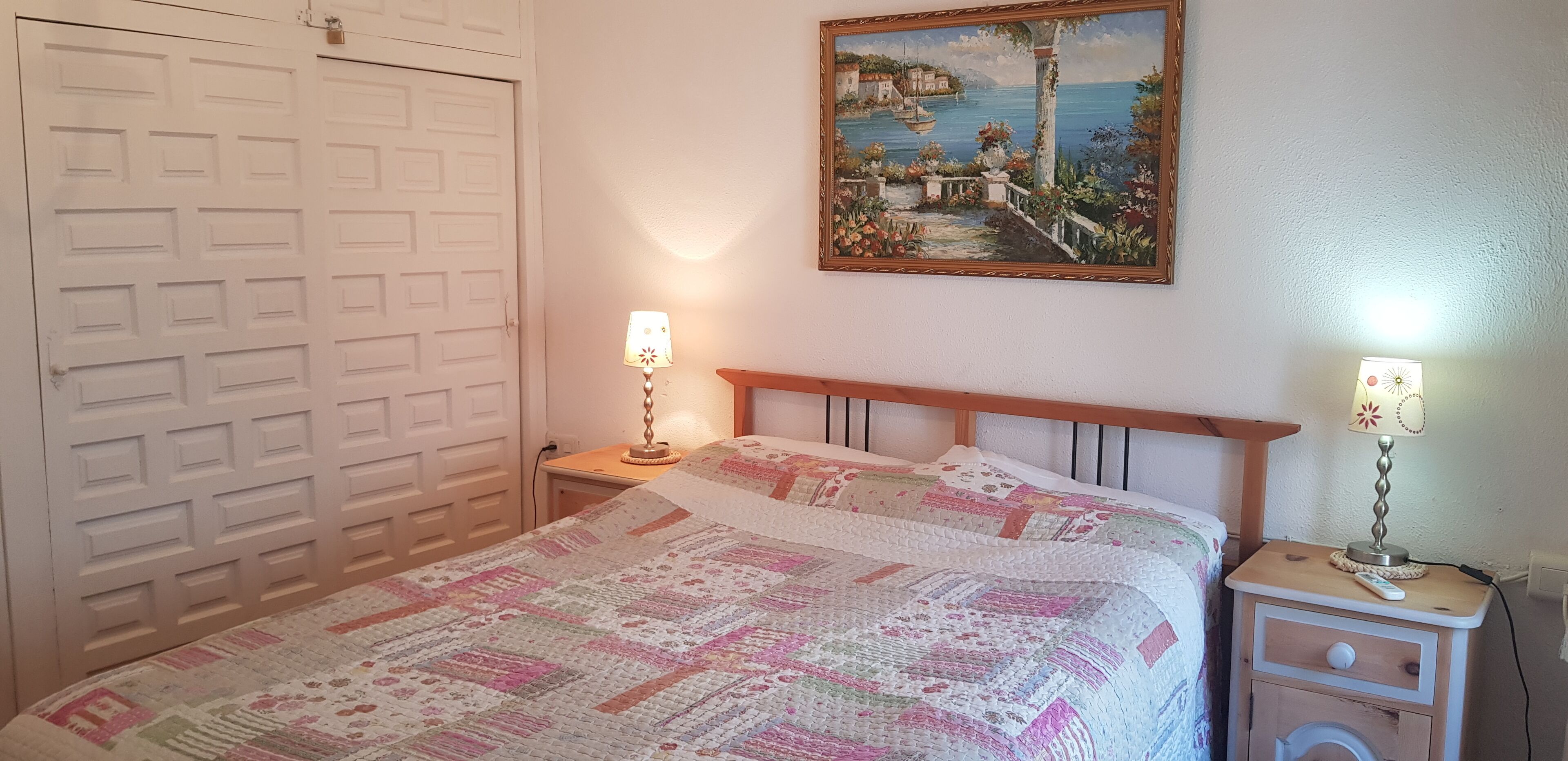 Una camera da letto con un letto, un comodino, una lampada, un quadro e una porta.