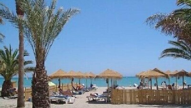 A beach with palm trees, sun loungers, and thatched umbrellas. - Burriana Beach 4 Mins Walk, Spanish Town House, 2 Pools - Gardens, WIFI, Air-Con (Burriana, Malaga)