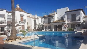 A swimming pool surrounded by white buildings with balconies, a palm tree, and a sign that reads "HOTEL". - Burriana Beach 4 Mins Walk, Spanish Town House, 2 Pools - Gardens, WIFI, Air-Con (Burriana, Malaga)