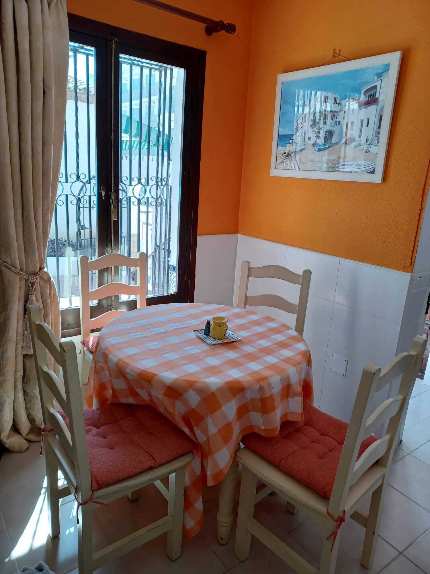 A dining area with a checkered tablecloth, wooden chairs, and a painting on the wall.