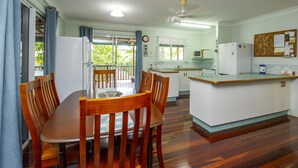 Un coin repas avec une table et des chaises en bois, une cuisine avec des meubles blancs et des appareils électroménagers, et un balcon offrant une vue sur la verdure.