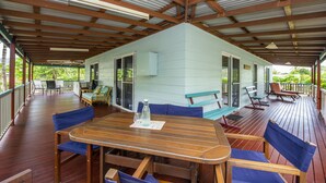 Une terrasse extérieure couverte, aménagée avec du mobilier en bois, notamment une table, des chaises et un banc.